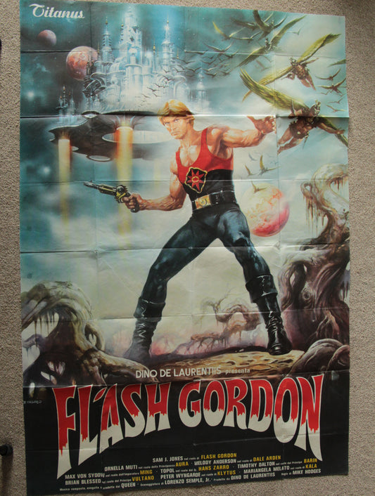 A vintage Flash Gordon movie poster displayed flat against a neutral background. The poster features the character Flash Gordon in a red and black costume, surrounded by sci-fi creatures, spaceships, planets, and a castle in the background, with the title 'FLASH GORDON' in large red letters at the bottom.